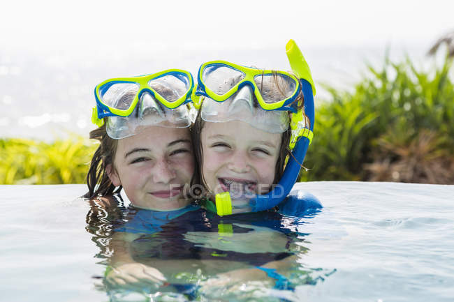 Adolescente rubia y hermano de edad elemental en la piscina sonriendo . - foto de stock