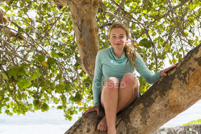 Adolescente chica sentada en el árbol y sonriendo . - foto de stock