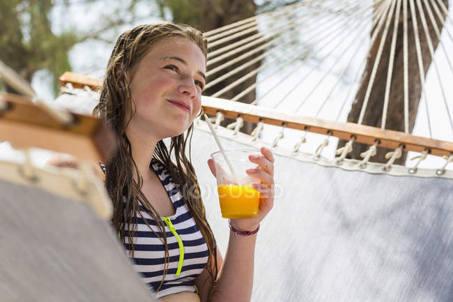 Blondes Teenager-Mädchen ruht in Hängematte und trinkt Fruchtgetränk. — Stockfoto