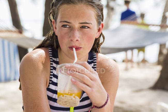 Blonde teenage girl resting in hammock drinking fruit drink. — Stock Photo