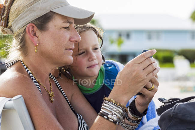 Madre e hijo preescolar mirando el teléfono inteligente en la playa . - foto de stock