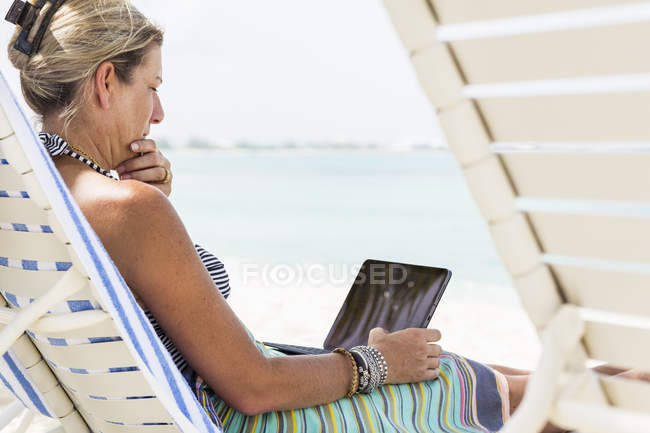 Ejecutiva femenina adulta usando computadora portátil en la playa, Isla Gran Caimán - foto de stock