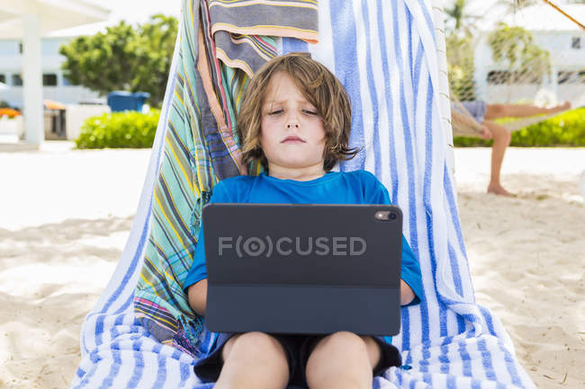 Preschooler boy using laptop in lounge chair at beach. — Stock Photo