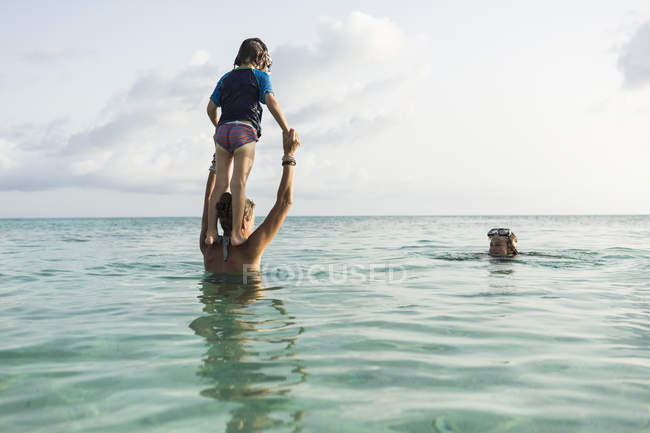 Дошкольный сын с материнских плеч, прыгающий в океан на закате
. — стоковое фото