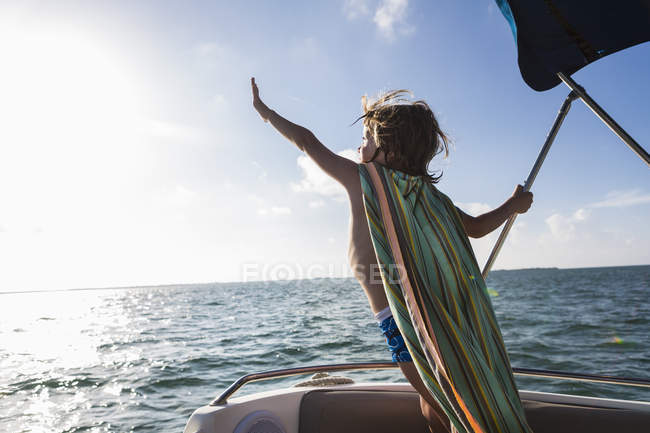 Маленький мальчик в плаще с полотенцами, склоняющийся вперед на лодке, остров Большой Кайман — стоковое фото