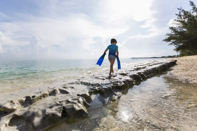 Little boy walking on rock formation with fins, Grand Cayman Island. — Stock Photo