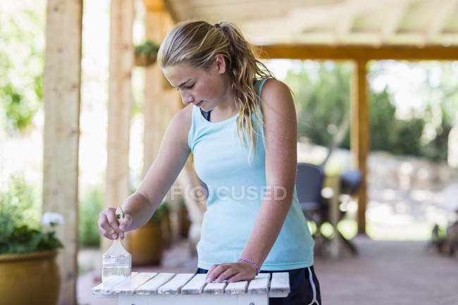 Loira adolescente pintura mobiliário ao ar livre em tinta branca . — Fotografia de Stock