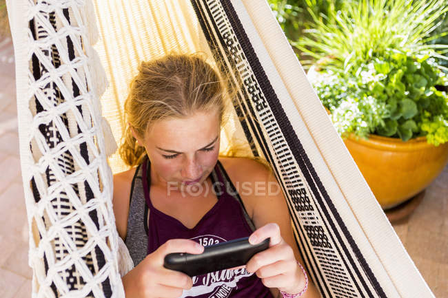 Blondes Teenie-Mädchen in Hängematte schaut aufs Smartphone. — Stockfoto