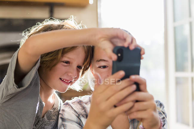 Adolescente e elementar irmão idade segurando smartphone e tomando selfie . — Fotografia de Stock