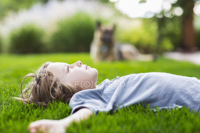 Menino da idade elementar deitado no exuberante gramado verde olhando para cima — Fotografia de Stock