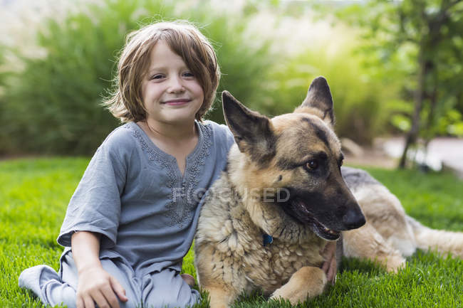 Menino idade elementar brincando com cão pastor alemão no gramado verde — Fotografia de Stock