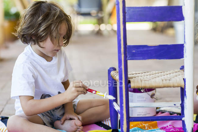 Elementary idade menino pintura cadeira no alpendre — Fotografia de Stock