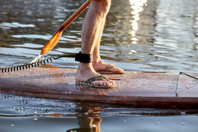 Nahaufnahme der Beine eines Mannes, der auf einem Paddelbrett auf Flusswasser steht — Stockfoto