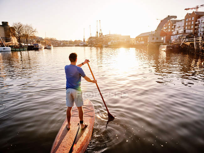 Uomo in piedi sul paddleboard sul fiume all'alba, vista posteriore — Foto stock