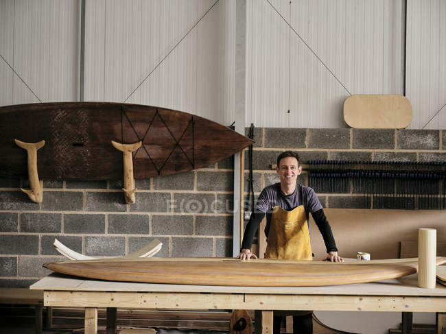 Porträt eines Mannes, der in der Werkstatt vor einem handgefertigten Holzpaddel steht — Stockfoto