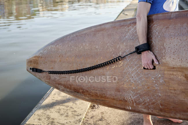 Close-up of man holding paddleboard next to river water on pier. — Stock Photo