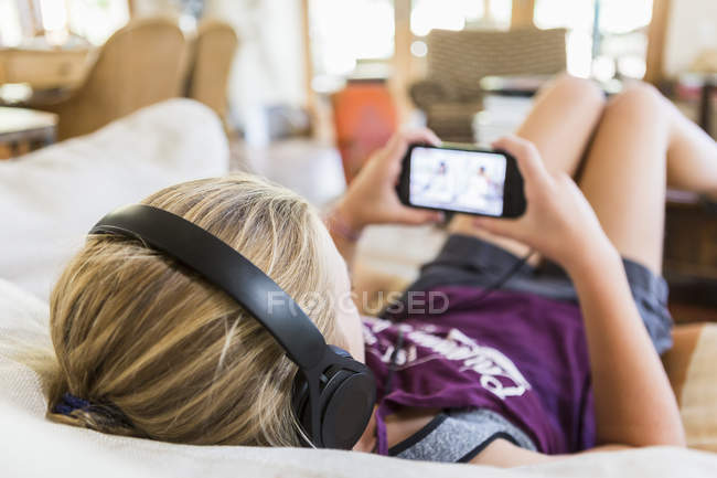 Вид спереду дівчини-підлітка вдома в навушниках і дивиться на екран смартфона — стокове фото