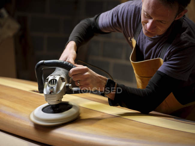 Paddleboard maker using sander in wood workshop — Stock Photo