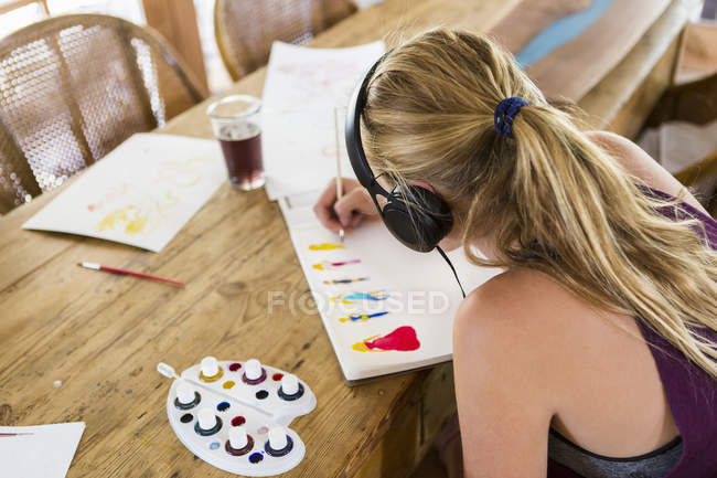 Teenage girl wearing headphones as doing watercolor painting in notebook — Stock Photo