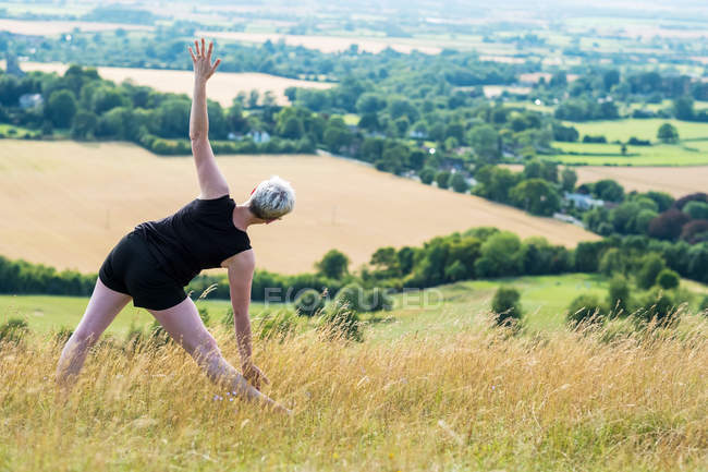 Vue arrière de la femme pratiquant le yoga en plein air sur la colline . — Photo de stock