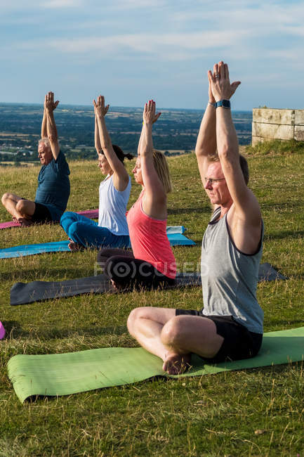 Gruppe von Frauen und Männern, die an einem Yoga-Kurs im Freien am Hang teilnehmen. — Stockfoto