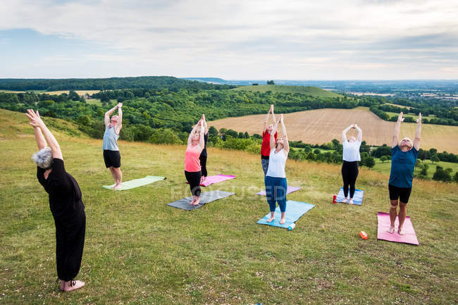 Gruppe von Frauen und Männern, die an einem Yoga-Kurs im Freien am Hang teilnehmen. — Stockfoto