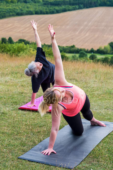 Two women taking part in outdoor yoga class on a hillside. — Stock Photo