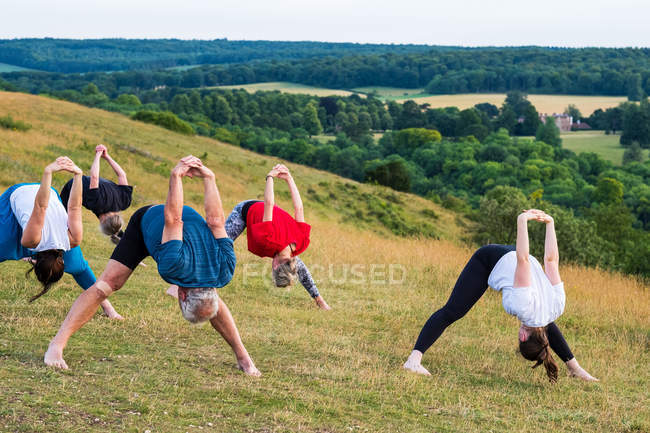 Група жінок і чоловіків, які беруть участь у відкритому класі йоги на схилі пагорба.. — стокове фото