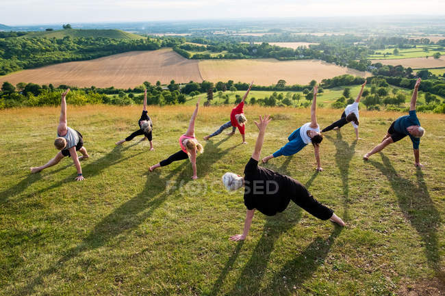 Group of women and men taking part in outdoor yoga class on a hillside. — Stock Photo