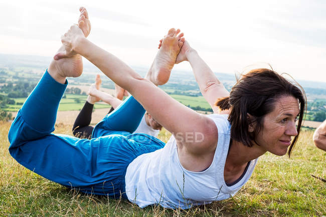 Mature woman taking part in outdoor yoga class on a hillside. — Stock Photo