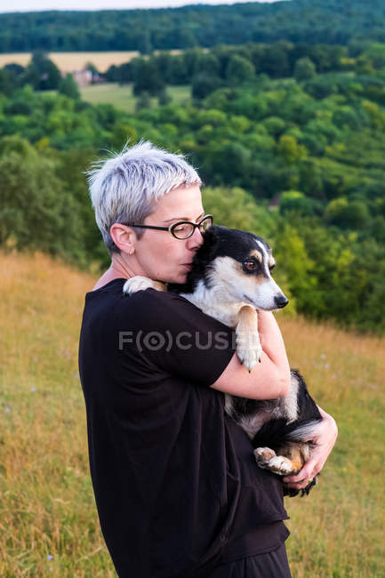 Femme aux cheveux gris court portant des lunettes et tenant un chien . — Photo de stock