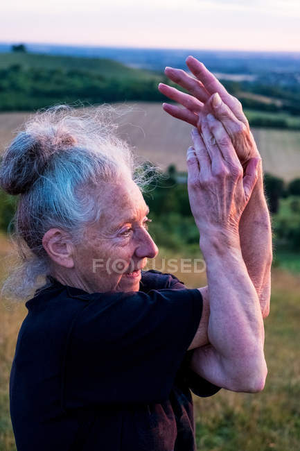 Senior woman taking part in outdoor yoga class on hillside. — Stock Photo