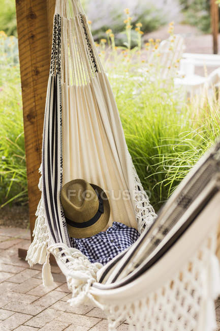 Cute elementary age boy covered with hat lying in hammock on porch — Stock Photo