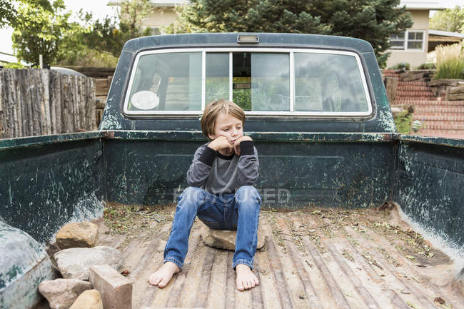 Portrait of elementary age boy sitting in bed of old pick up truck — Stock Photo