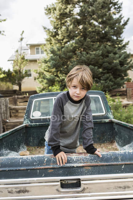 Portrait d'un garçon d'âge élémentaire posant dans le lit d'une vieille camionnette — Photo de stock