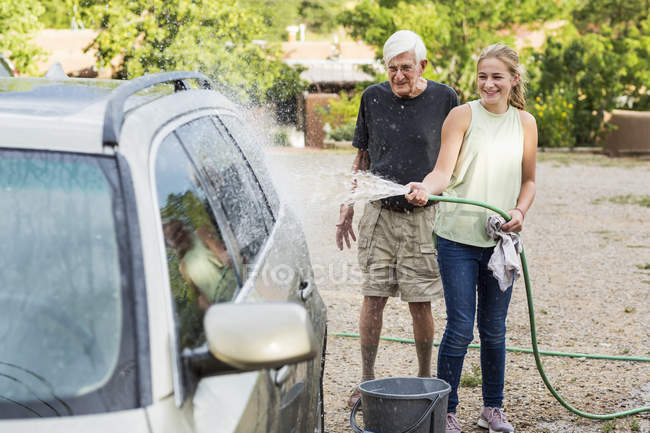 Avô sênior e neta adolescente lavar carro juntos na entrada de carro — Fotografia de Stock