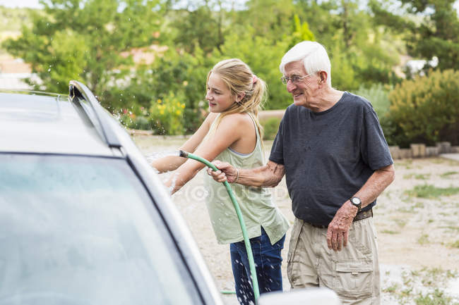 Abuelo mayor y nieta adolescente lavando el coche juntos en la entrada - foto de stock