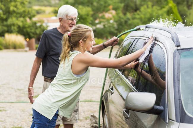 Senior Opa und Teenager-Enkelin waschen gemeinsam Auto in Einfahrt — Stockfoto