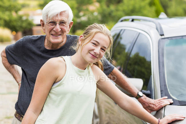 Grand-père aîné et petite-fille adolescente posant tout en lavant la voiture ensemble dans l'allée — Photo de stock
