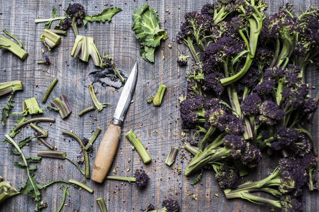 High angle close-up of purple sprouting broccoli and knife with wooden handle. — Stock Photo