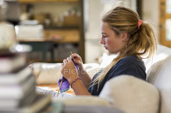 Side view of focused teenage girl knitting on sofa in living room — Stock Photo