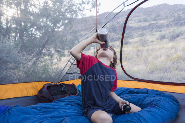 Junge im Grundschulalter trinkt aus Wasserflasche im Zelt — Stockfoto
