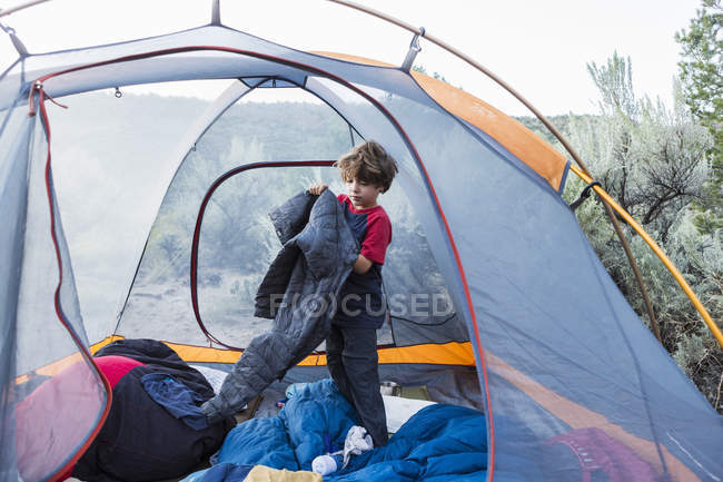 Elementary age boy getting dressed in outdoor touristic tent — Stock Photo
