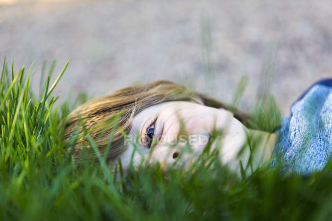 Retrato de menino de idade elementar sorridente deitado na grama verde — Fotografia de Stock