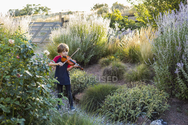 Elementary age boy playing violin outside in garden — Stock Photo