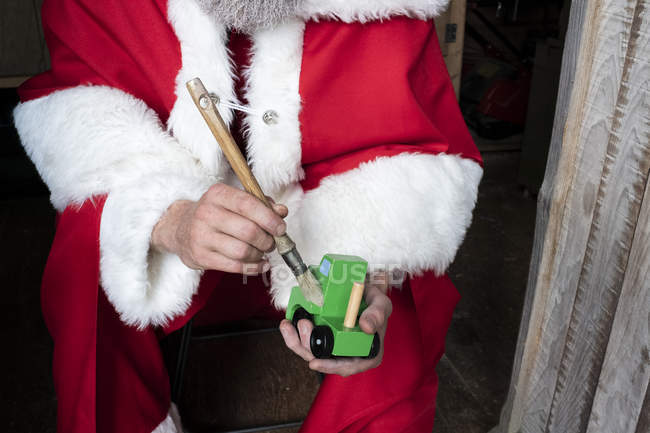 Close-up of man wearing Santa Claus costume holding and brushing wooden toy car. — Stock Photo