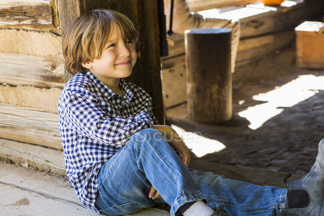 Porträt eines Jungen im Grundschulalter, der in einer Holzscheune sitzt — Stockfoto