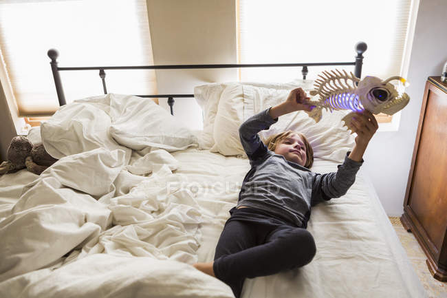 Хлопчик початкового віку грає з рибною іграшкою на ліжку — стокове фото