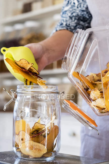 Close-up of person standing in a kitchen, placing slices of dried fruit into glass jar. — Stock Photo