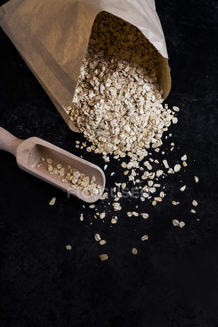 High angle close-up of paper bag with oats and wooden spoon on dark background. — Stock Photo
